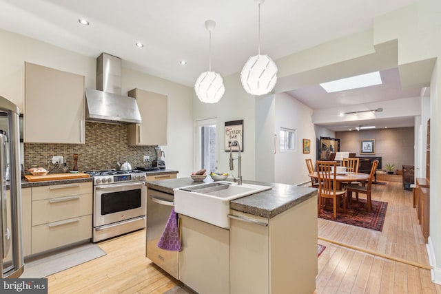 kitchen with light wood-type flooring, cream cabinetry, stainless steel appliances, wall chimney exhaust hood, and a sink