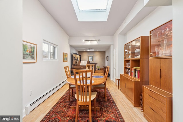 dining area featuring a baseboard heating unit, a skylight, and light wood finished floors