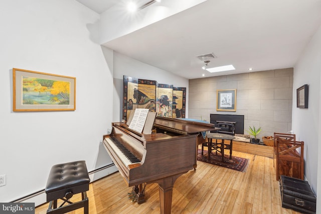 interior space featuring visible vents, a skylight, light wood finished floors, baseboard heating, and a wood stove