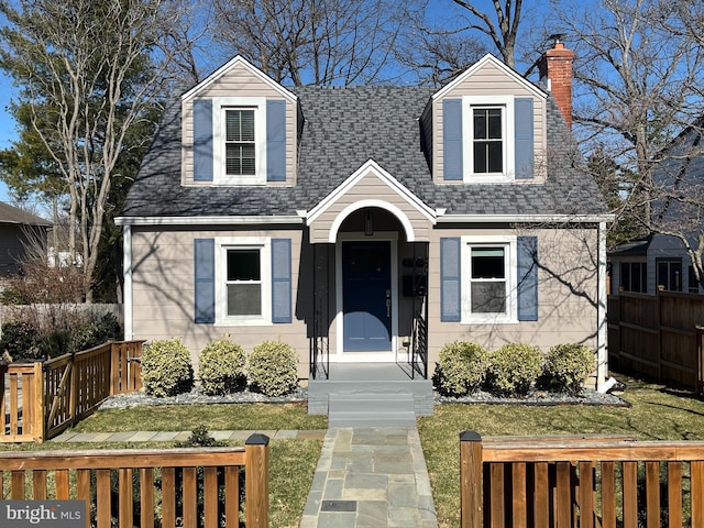 cape cod-style house with a front lawn, fence private yard, a chimney, and a shingled roof