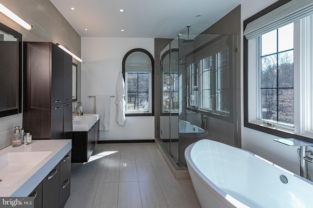 bathroom with a shower stall, two vanities, recessed lighting, a soaking tub, and a sink