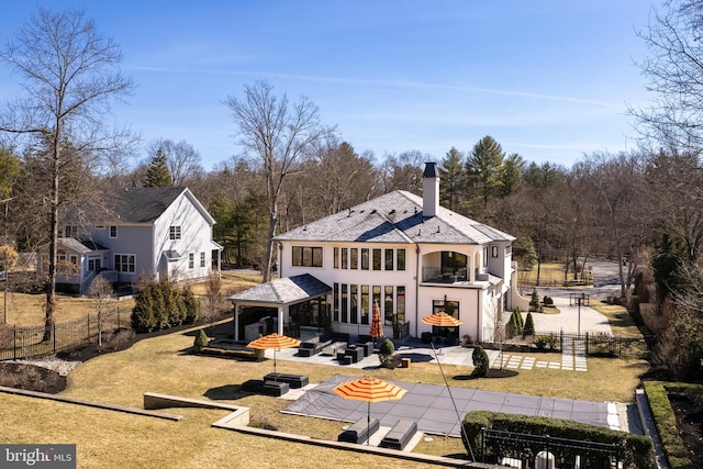 back of house featuring a balcony, a chimney, fence private yard, a patio area, and a lawn