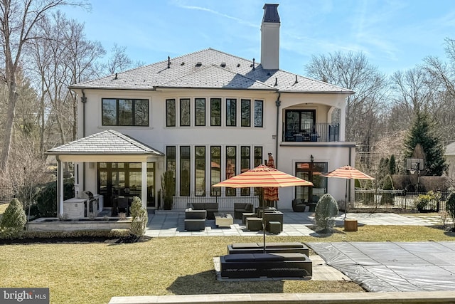 back of property with fence, an outdoor hangout area, a balcony, a chimney, and a patio area