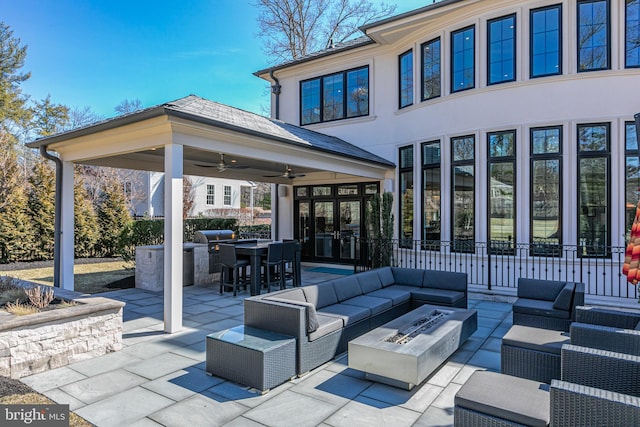 view of patio / terrace with fence, exterior kitchen, outdoor dining area, ceiling fan, and an outdoor living space with a fire pit