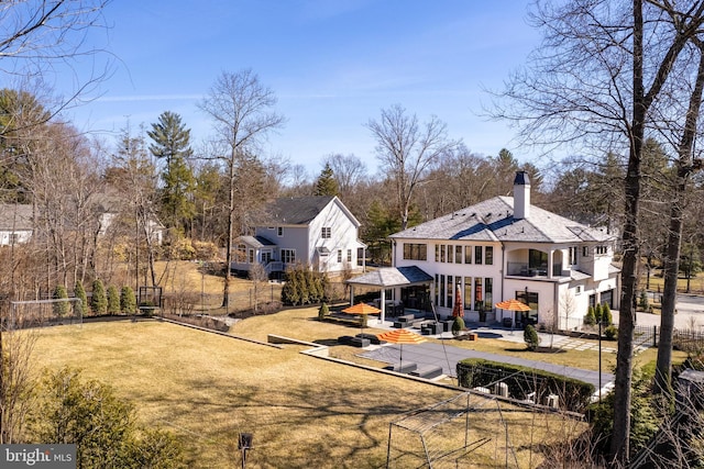 rear view of property with a wooden deck, fence private yard, a lawn, a chimney, and a balcony