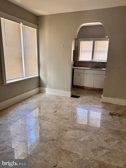 spare room featuring arched walkways, baseboards, and a sink