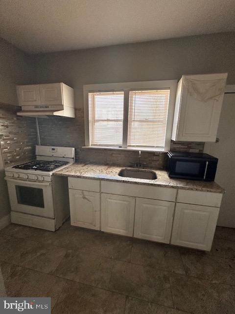 kitchen featuring a sink, gas range gas stove, backsplash, white cabinets, and black microwave