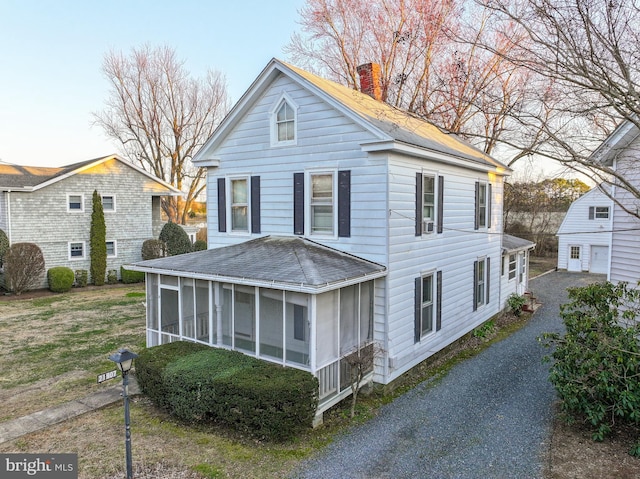 view of front of home featuring a shingled roof, a sunroom, and a chimney