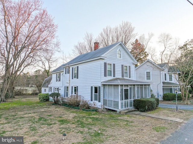 view of front of home with a chimney, a front lawn, and a sunroom