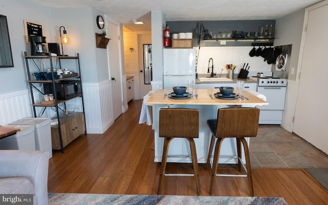 kitchen featuring a sink, a wainscoted wall, white appliances, and dark wood-style floors