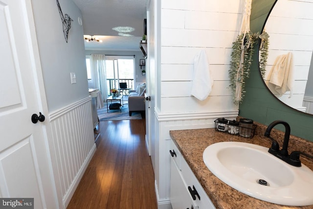 bathroom with ornamental molding, wainscoting, wood finished floors, a decorative wall, and vanity