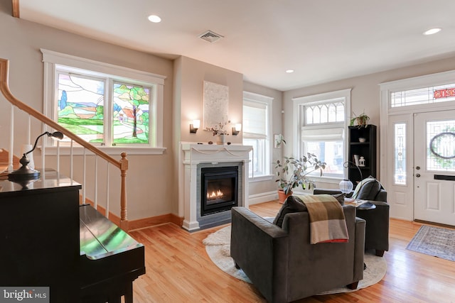 living room with visible vents, a glass covered fireplace, recessed lighting, light wood-style floors, and stairs