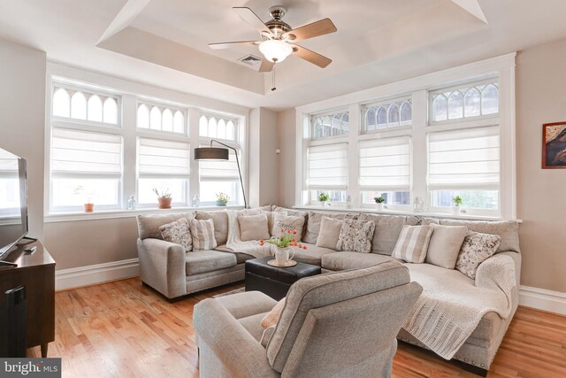 living room featuring a raised ceiling, light wood-style flooring, baseboards, and ceiling fan