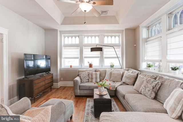 living area featuring a tray ceiling, baseboards, visible vents, and wood finished floors