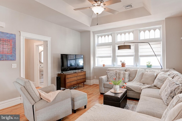 living area featuring visible vents, a raised ceiling, light wood-type flooring, and baseboards