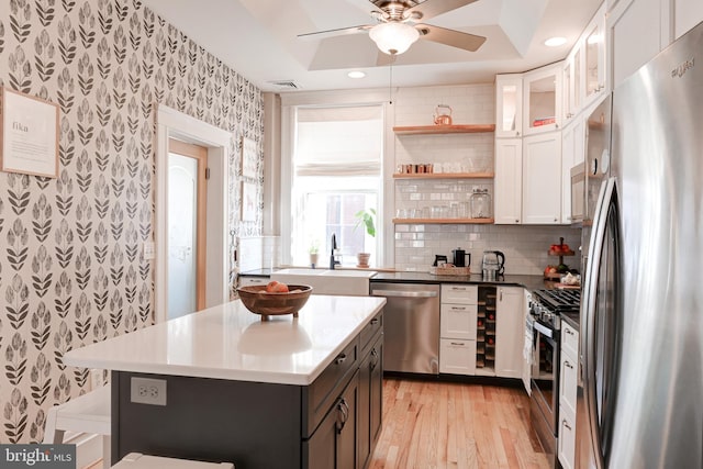 kitchen with a sink, wallpapered walls, appliances with stainless steel finishes, white cabinetry, and open shelves