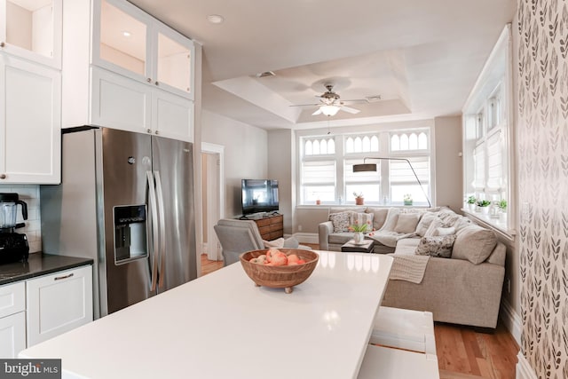 kitchen featuring light wood-type flooring, glass insert cabinets, white cabinetry, a raised ceiling, and stainless steel fridge