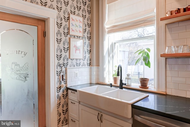 kitchen with wallpapered walls, white cabinets, a wealth of natural light, and a sink