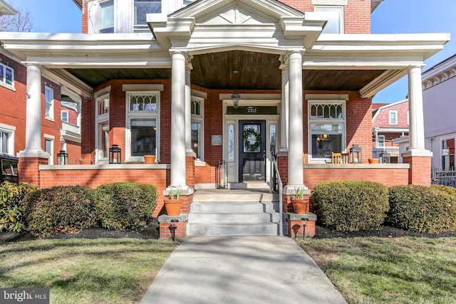 doorway to property with a porch and brick siding