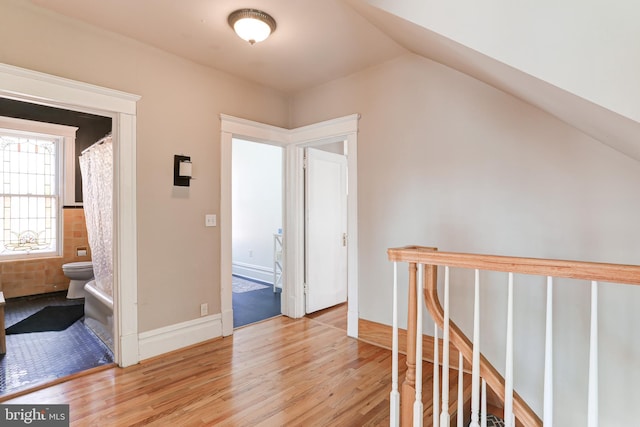 hallway with baseboards, an upstairs landing, light wood-style floors, and vaulted ceiling