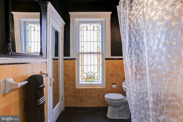 bathroom featuring a shower with curtain, tile walls, toilet, and a healthy amount of sunlight