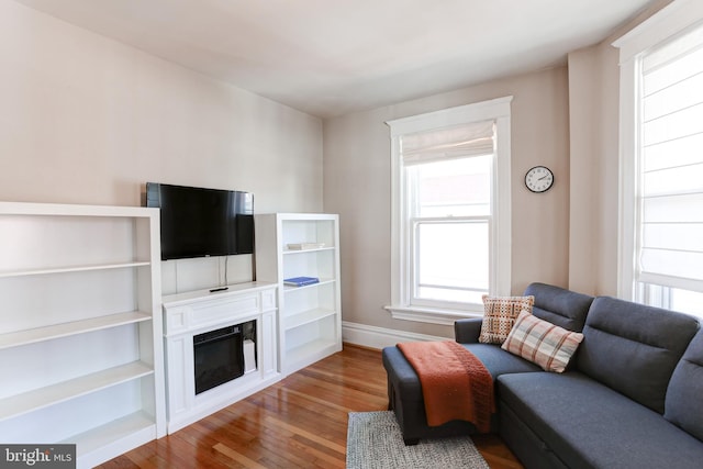 living room with a glass covered fireplace, wood finished floors, and baseboards