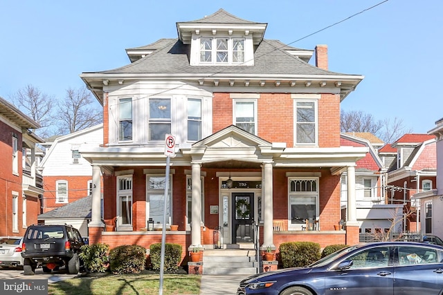 traditional style home featuring brick siding, a porch, and roof with shingles