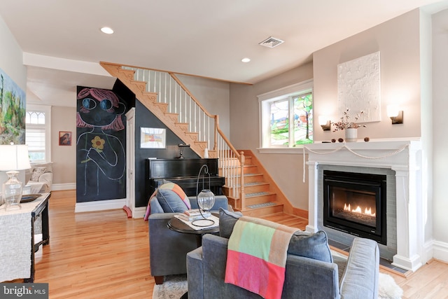 living room featuring a glass covered fireplace, light wood-style flooring, stairs, and a wealth of natural light