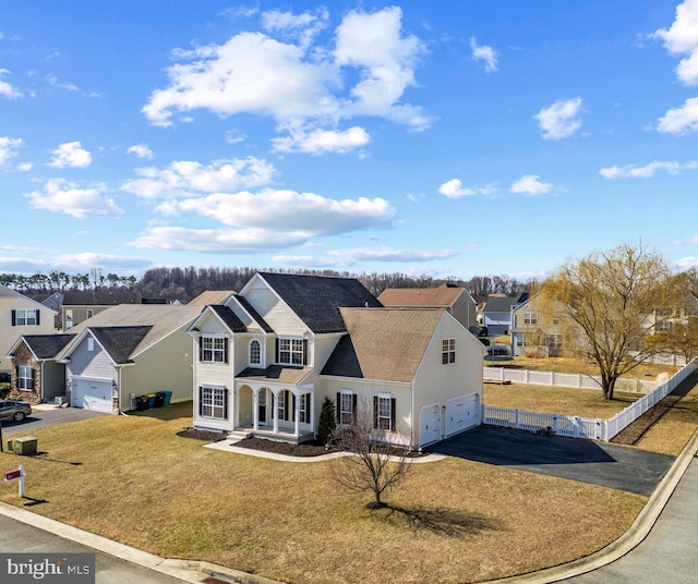 view of front of house with a front yard, fence, driveway, an attached garage, and a residential view