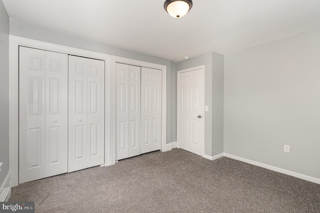 unfurnished bedroom featuring two closets, baseboards, and dark carpet