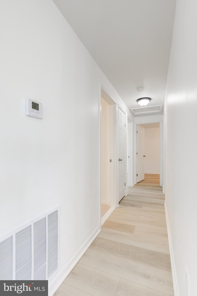 corridor featuring visible vents, baseboards, and light wood-style flooring