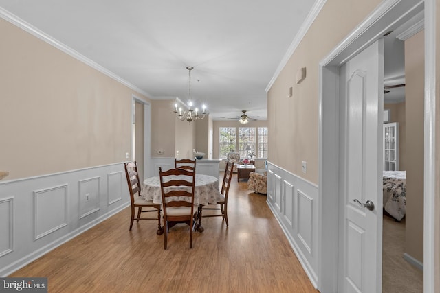 dining room featuring wood finished floors, an inviting chandelier, ornamental molding, and a decorative wall