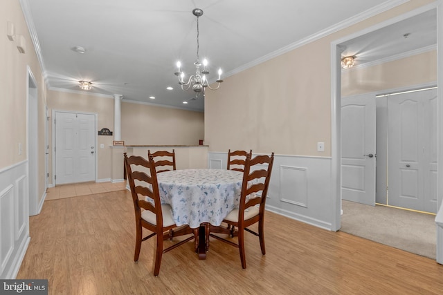 dining room with crown molding, light wood-type flooring, wainscoting, a decorative wall, and ornate columns