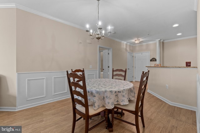 dining room featuring crown molding, light wood-style flooring, a decorative wall, and wainscoting