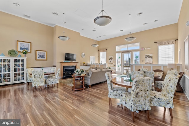 dining space featuring wood finished floors, visible vents, a high ceiling, a glass covered fireplace, and crown molding