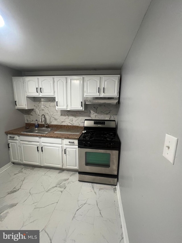 kitchen with marble finish floor, under cabinet range hood, a sink, dark countertops, and stainless steel gas range