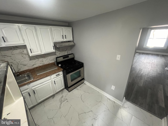 kitchen featuring stainless steel range with gas cooktop, under cabinet range hood, marble finish floor, white cabinetry, and a sink