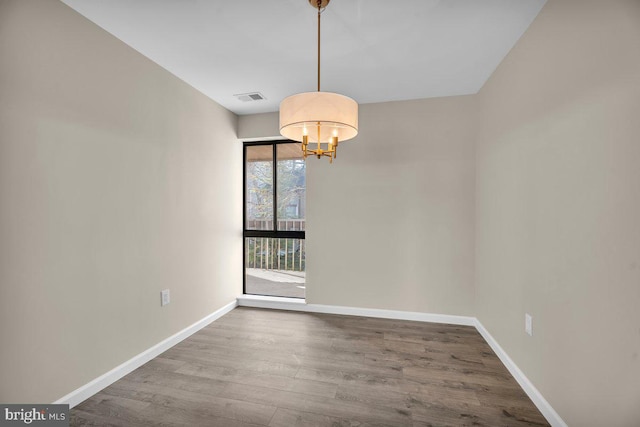 unfurnished room with wood finished floors, visible vents, a chandelier, and baseboards