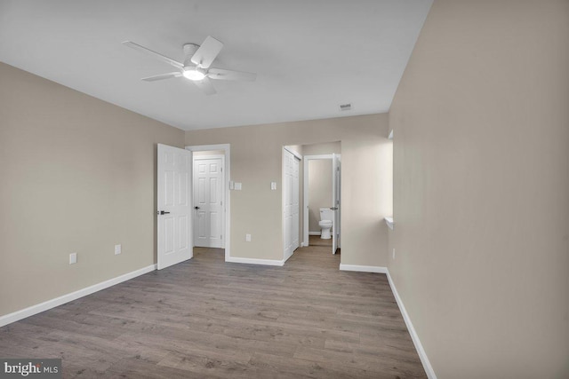 unfurnished bedroom with visible vents, connected bathroom, baseboards, wood finished floors, and a ceiling fan