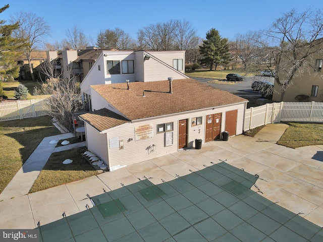 view of front facade with a patio area, roof with shingles, and fence