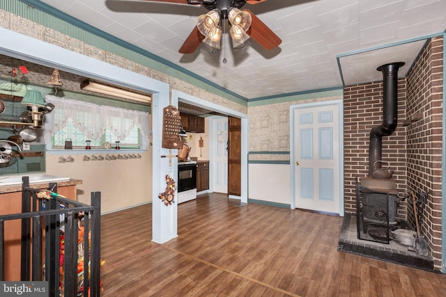 living area with a ceiling fan, a wood stove, wood finished floors, and wallpapered walls