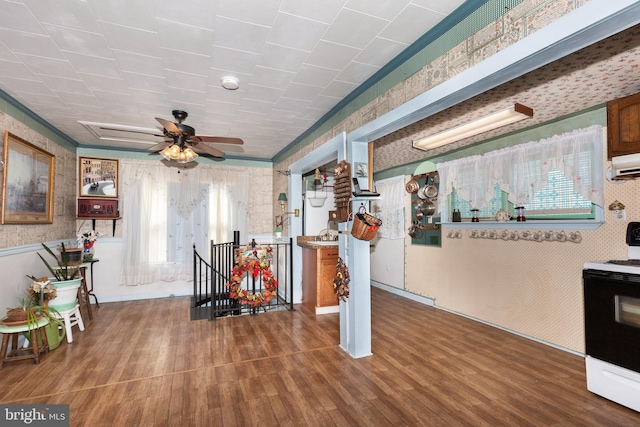 interior space with ceiling fan, wood finished floors, electric range oven, and wallpapered walls