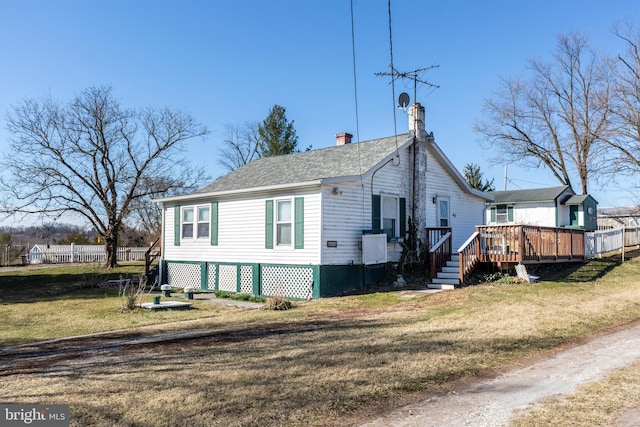 view of side of home featuring a shingled roof, fence, a wooden deck, a chimney, and a yard