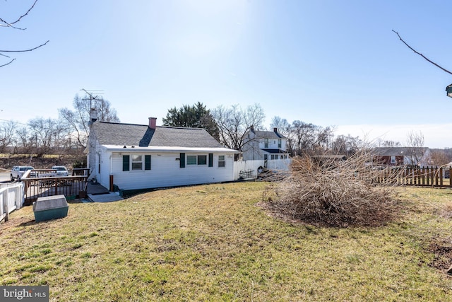 rear view of house with a lawn, a deck, a chimney, and fence