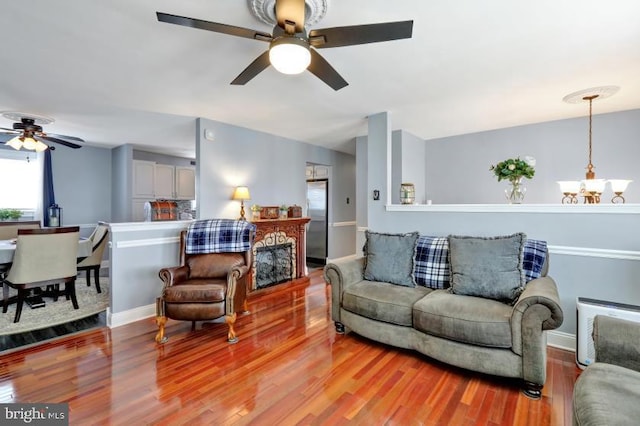 living room with ceiling fan with notable chandelier, wood finished floors, and baseboards