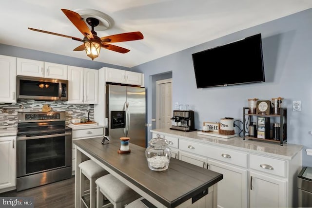 kitchen with backsplash, ceiling fan, wood finished floors, white cabinets, and stainless steel appliances