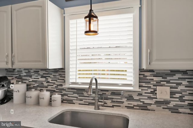 kitchen featuring decorative light fixtures, decorative backsplash, light stone counters, and a sink