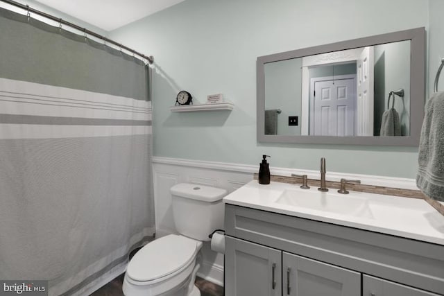 bathroom featuring a wainscoted wall, toilet, vanity, and a shower with curtain