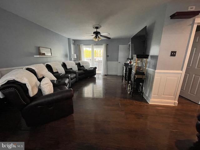 living room with a ceiling fan, dark wood-style flooring, and wainscoting