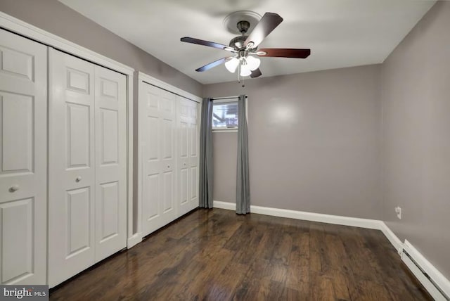 unfurnished bedroom featuring two closets, baseboards, baseboard heating, ceiling fan, and dark wood-style flooring